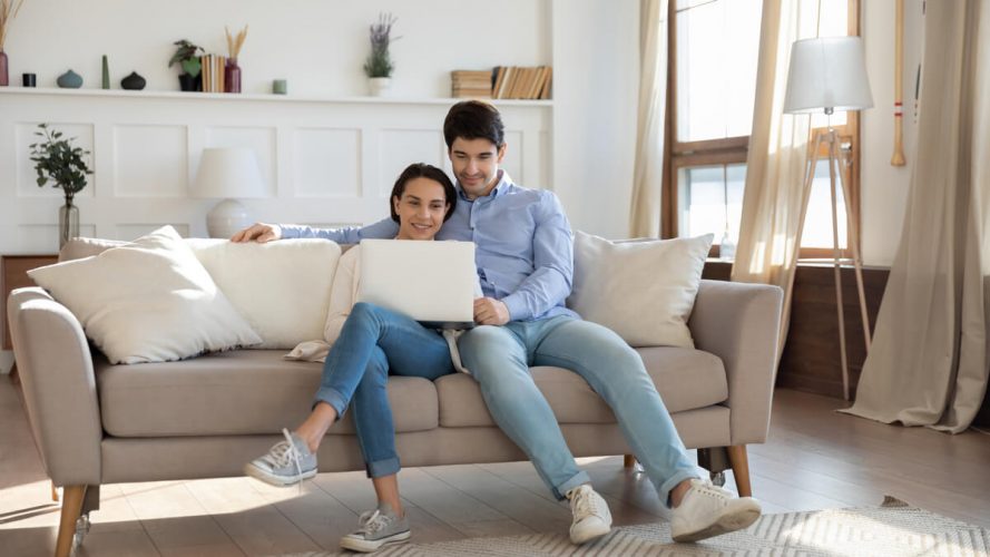 Man and woman sit on couch looking at a laptop