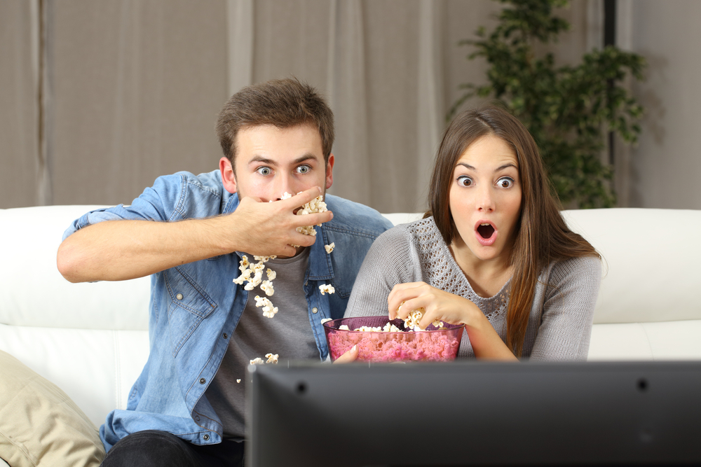 Man and woman eat popcorn and watch television